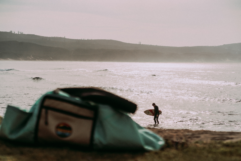 Surfer walking a misty beach with an Outeniqua Bound bag in the foreground
