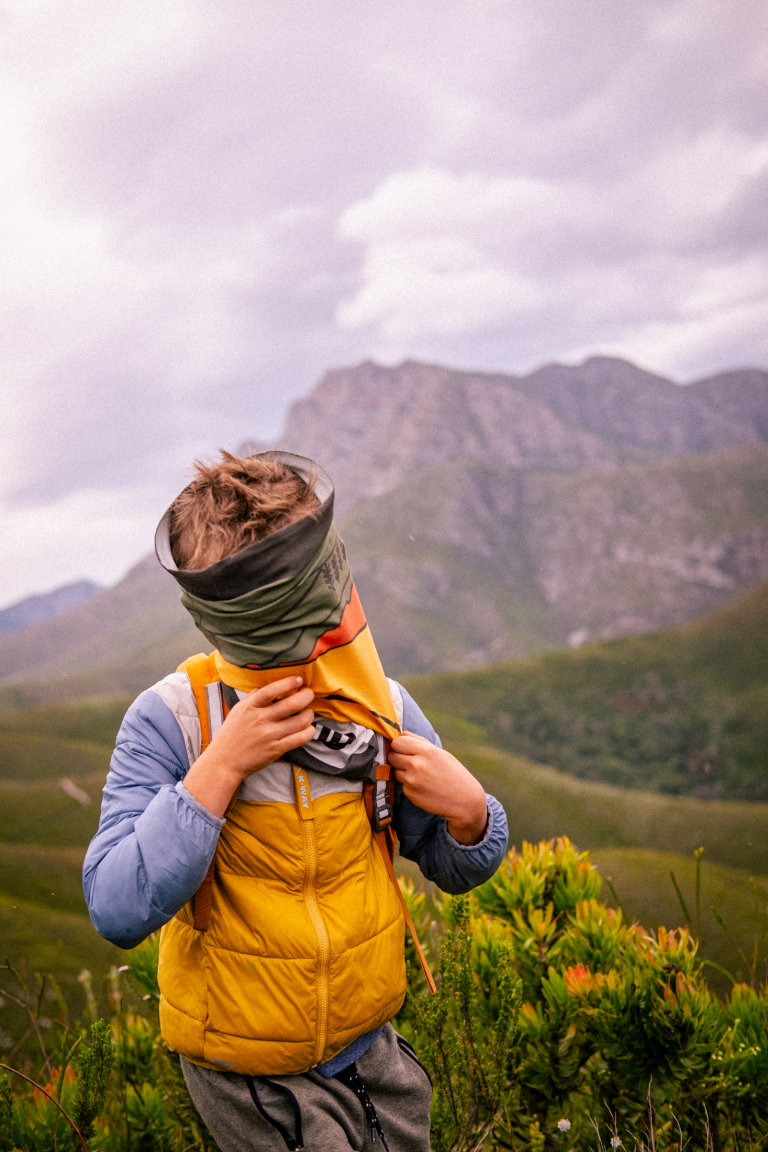 Hiker wearing a George Peak Buff over their face in the mountains
