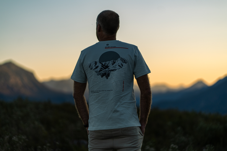 Man in a white Summit Tee looking out over the mountains at sunset