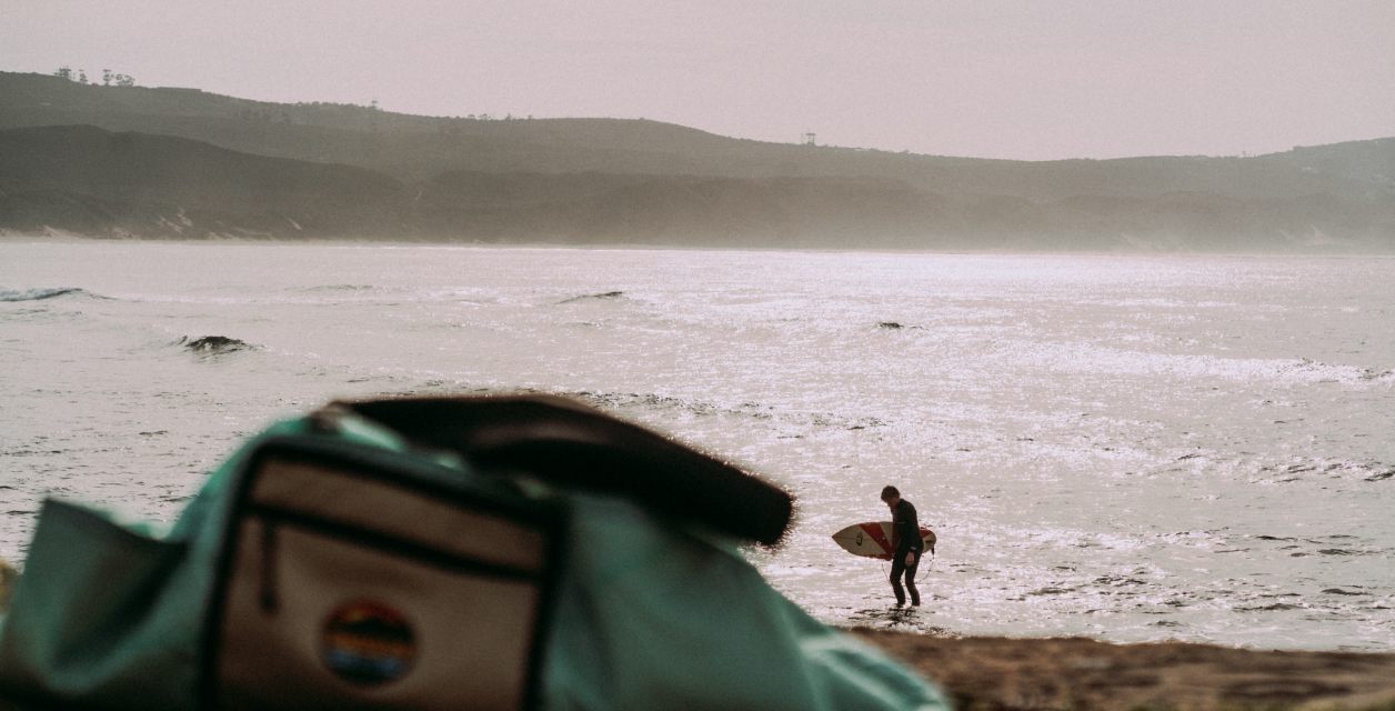 Surfer walking a misty beach with an Outeniqua Bound bag in the foreground