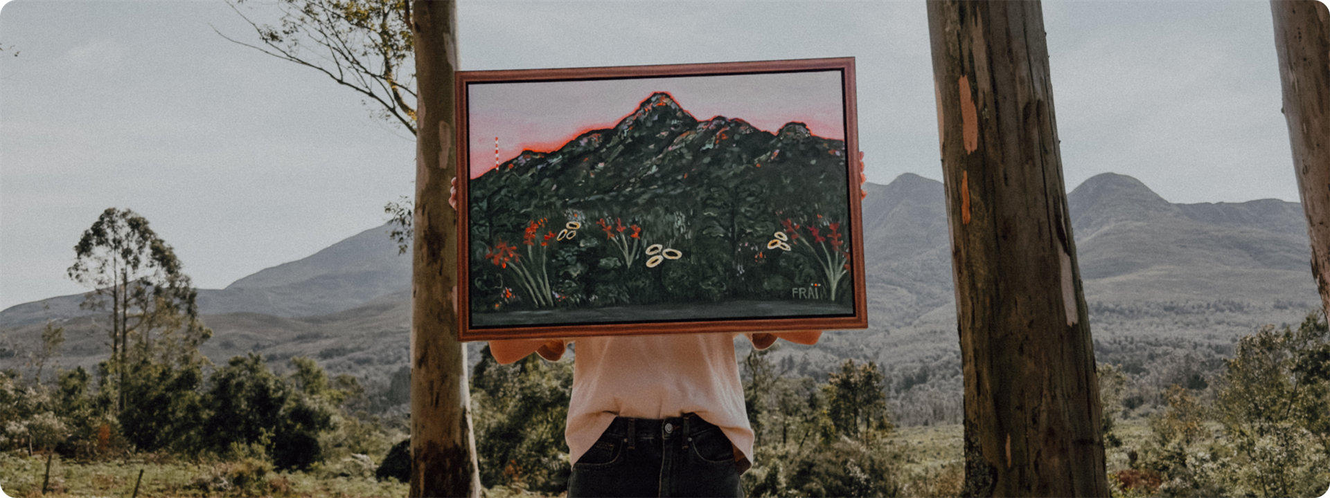 Framed mountain painting held up between trees